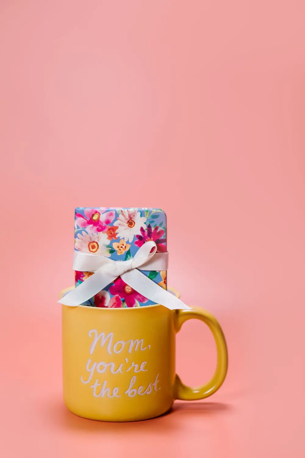 Taza amarilla «Mom, you're the best» con regalo sobre fondo rosado